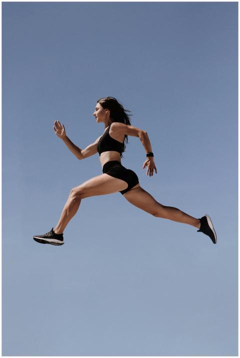 Energetic woman in athletic wear leaping against c
