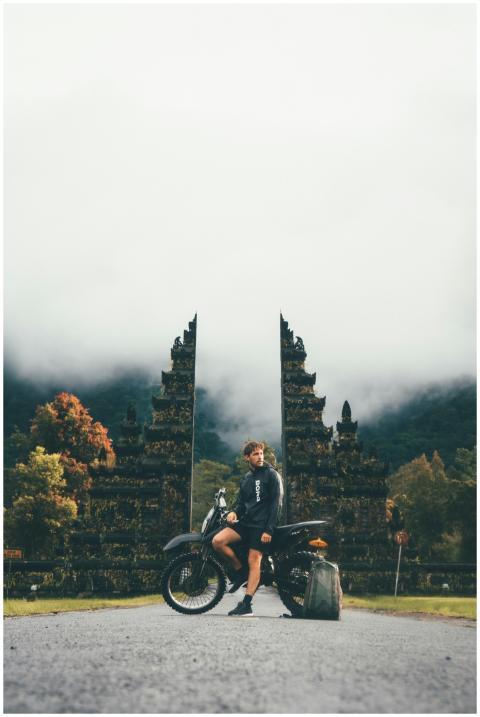 Man posing with motorcycle at iconic Bali temple g