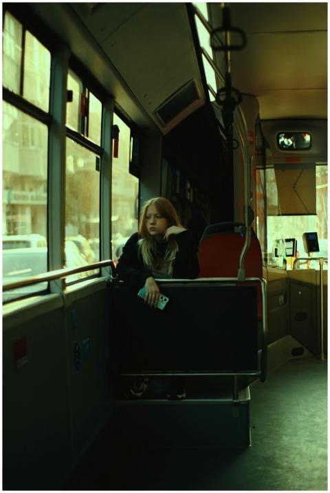 A woman sits alone in an urban bus, reflecting whi