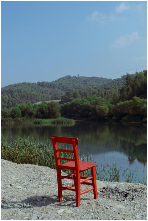 A lone red chair by a reflective lake, surrounded