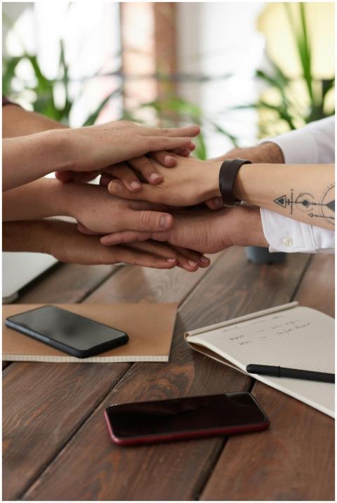 Hands from a diverse team stack on a table symboli