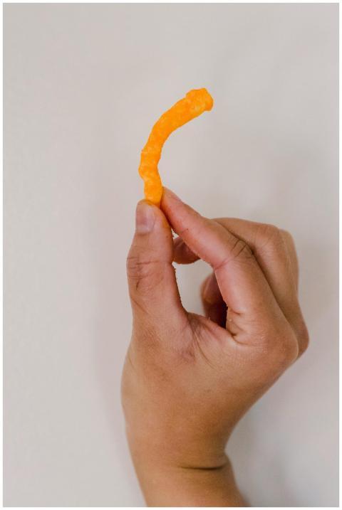 A hand holds a crispy orange cheese puff with a ne