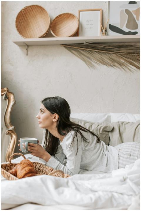 Woman relaxing in bed with coffee and croissants,