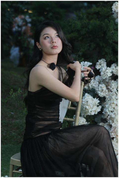 A woman in a black dress poses elegantly on a chai