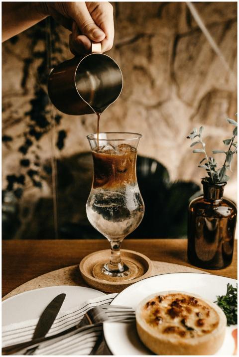 Hand pouring iced coffee into a glass on a table w