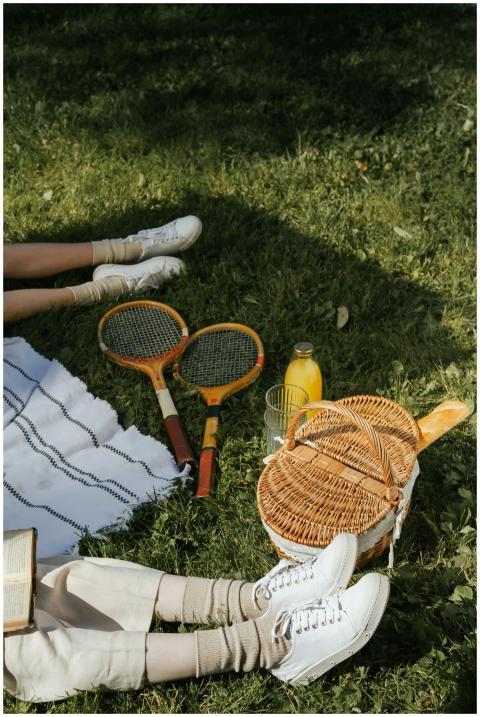 Outdoor picnic setup with tennis rackets, basket,