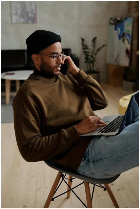 Young man multitasking at home using laptop and sm
