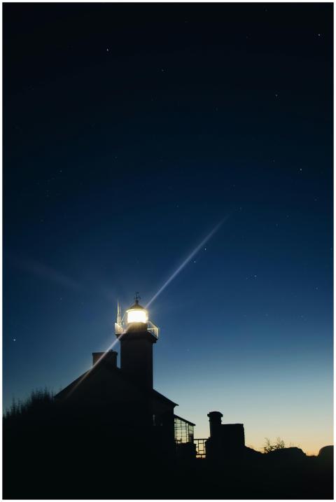 A silhouetted lighthouse illuminated at twilight b