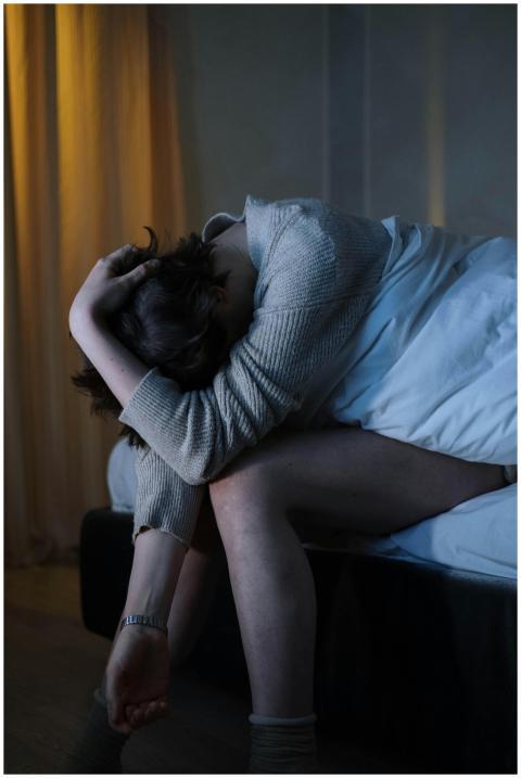 A woman sits on her bed, experiencing anxiety and