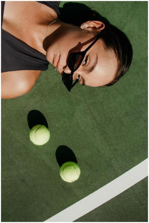 Woman in sunglasses lying on a tennis court with t