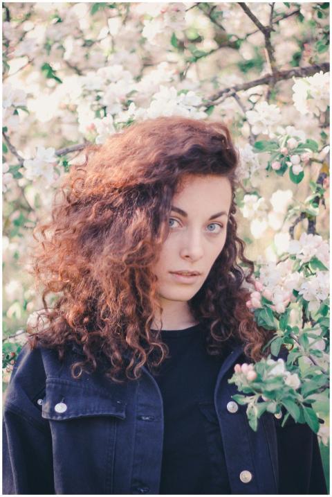 A woman with curly hair stands amid cherry blossom