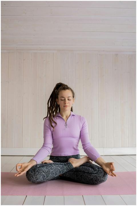 A woman sits cross-legged on a pink yoga mat medit