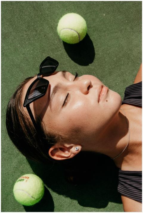 A young woman with sunglasses relaxes on a tennis