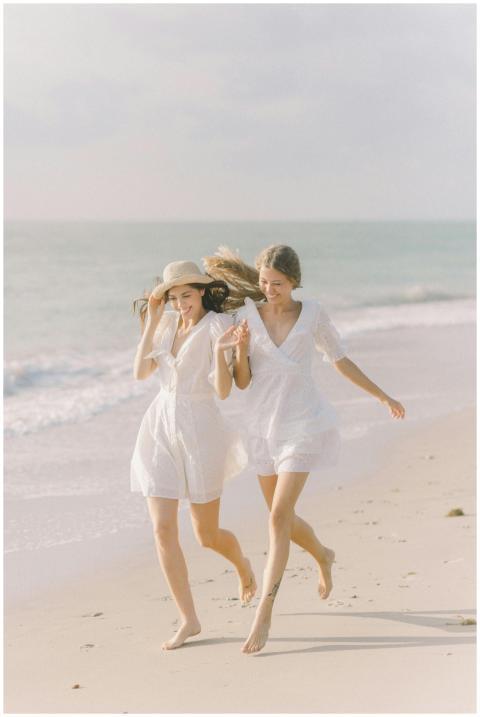 Two women in white dresses running happily along a