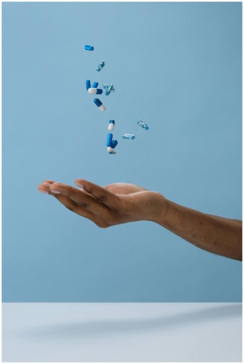 A hand catching blue pills midair against a light