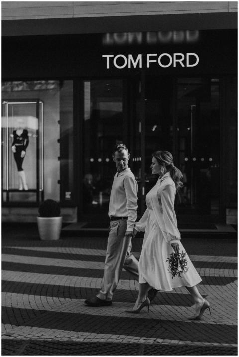 A stylish couple walks hand in hand in front of To