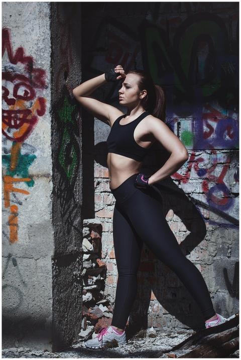 A fit woman in sportswear poses by a vibrant graff