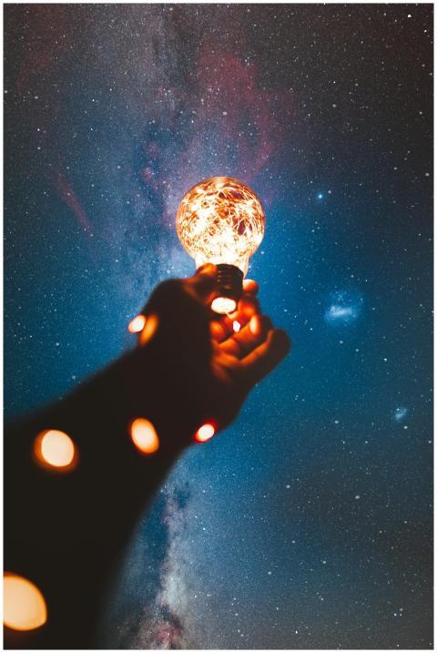 A hand holds a glowing bulb into the Milky Way nig