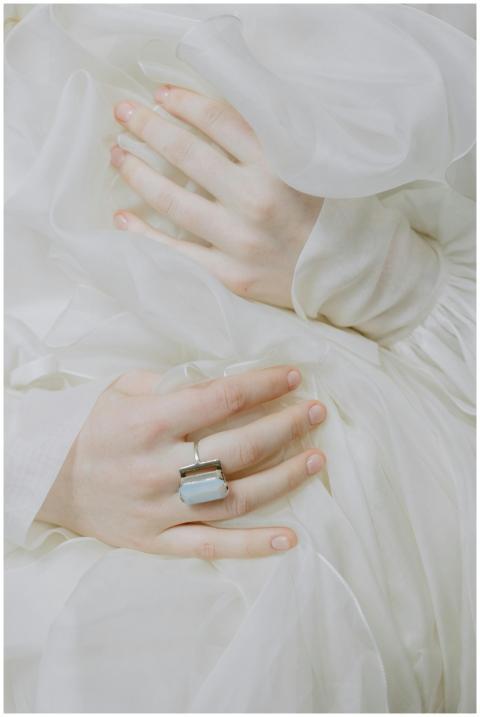 Close-up of hands with a gemstone ring against whi