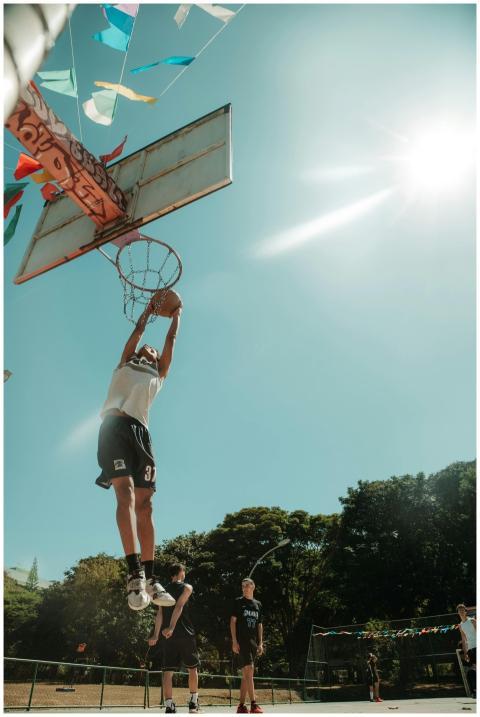 Athlete mid-air dunking under a bright blue sky in