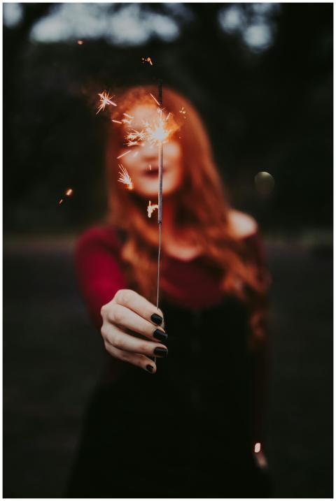 A woman holds a lit sparkler outdoors, creating a