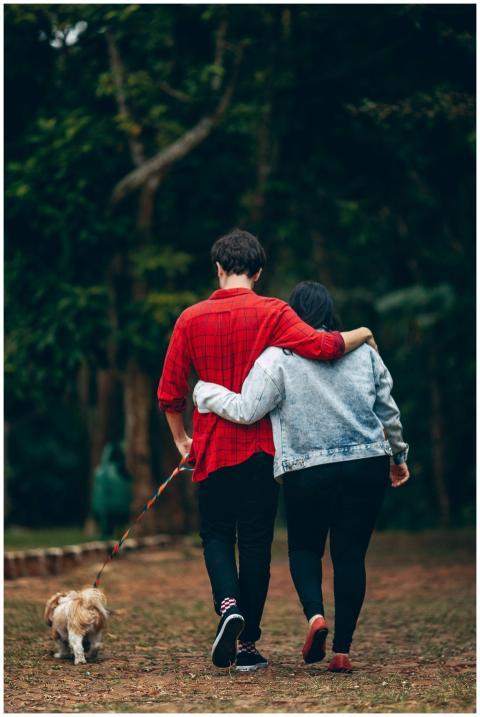 Couple walking with a Shih Tzu in a lush park, emb