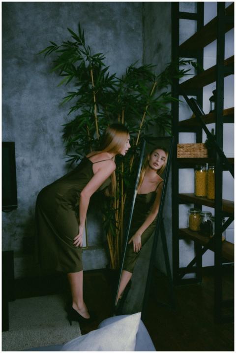 A woman in a green dress gazes into a mirror, surr