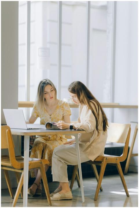 Two women collaborating over a laptop and book in