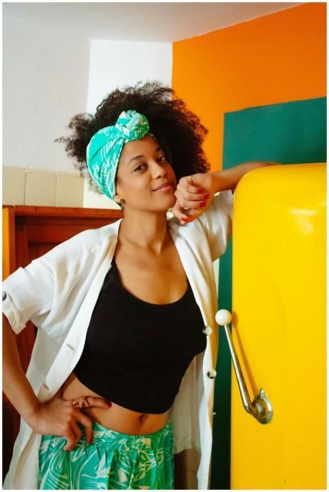 Woman with curly hair and headscarf smiling in a v