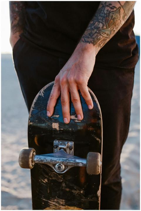 A tattooed hand gripping a skateboard on a sunny b