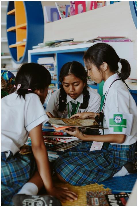 Three girls in school uniforms enjoying reading bo