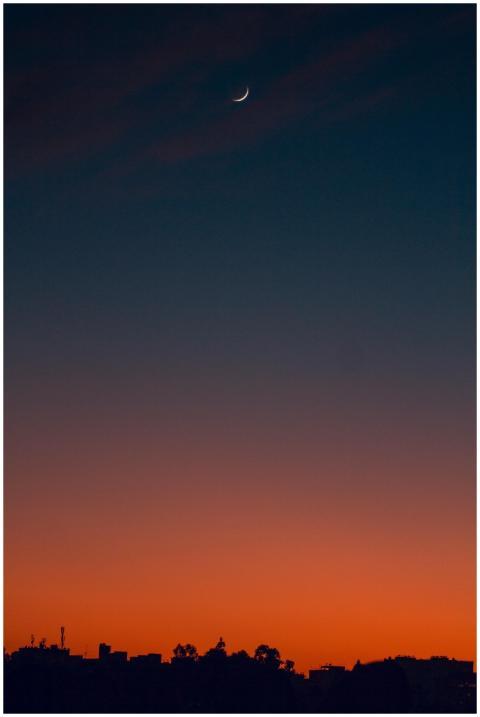 A serene crescent moon in a colorful dusk sky abov
