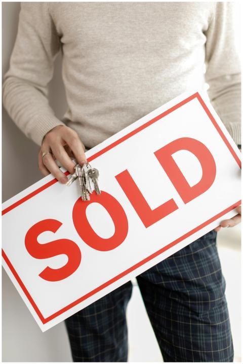 Close-up of a realtor holding a sold sign and keys