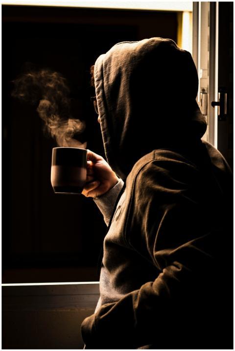 A person in a hoodie enjoys a steaming cup of coff