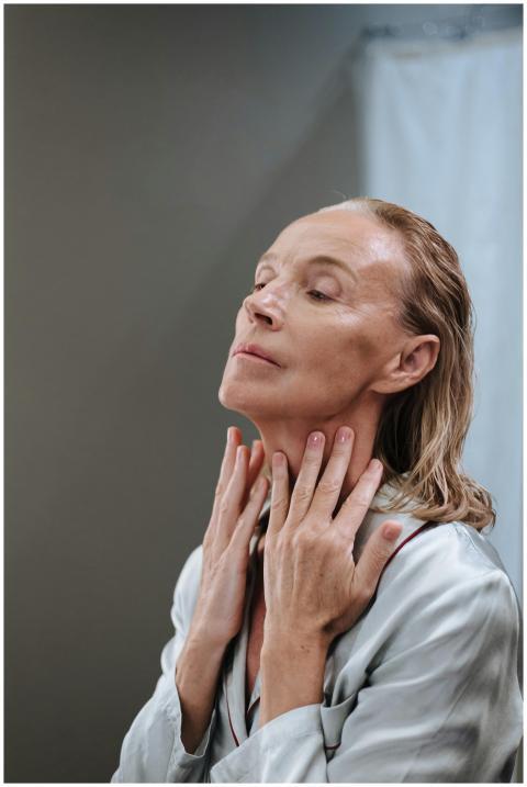 Elderly woman in bathroom applying skincare, focus