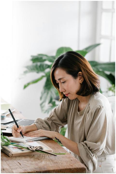 Woman sitting indoors writing in a notebook with g
