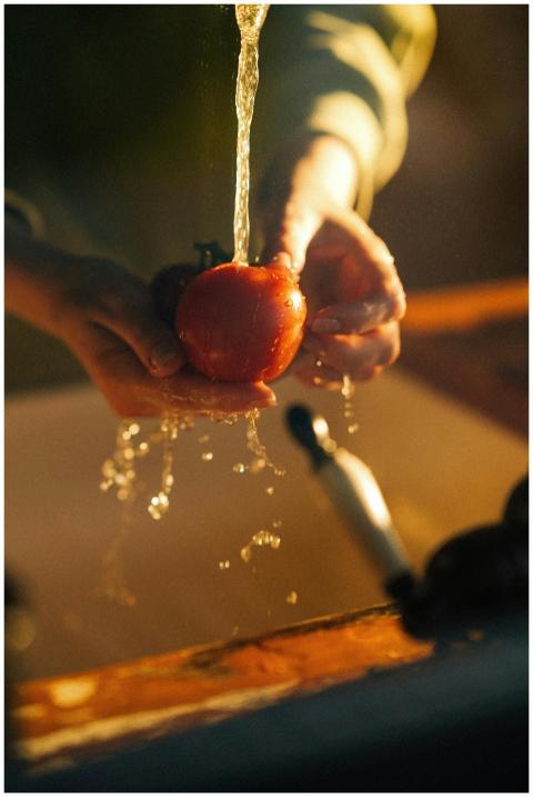 A person washing a fresh tomato under a faucet in