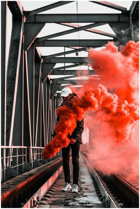 Man holding orange smoke bomb on railway bridge, c