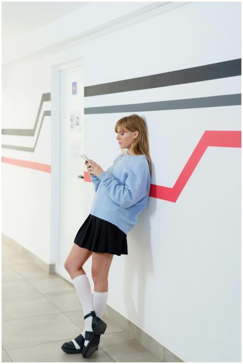 Young woman leans against a wall using smartphone,