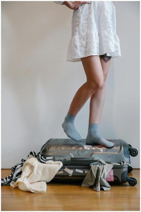 A woman attempts to close an overloaded suitcase b