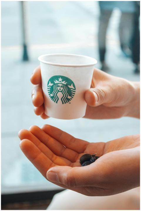 Hand holds a Starbucks cup and coffee beans, symbo