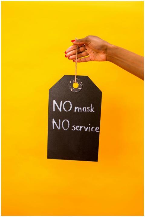 A hand holds a black 'No Mask, No Service' sign ag