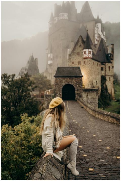 A woman sits outside Eltz Castle in foggy Wiersche