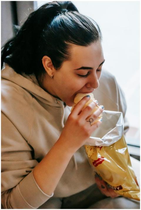 Woman enjoying a bag of potato chips indoors, indu