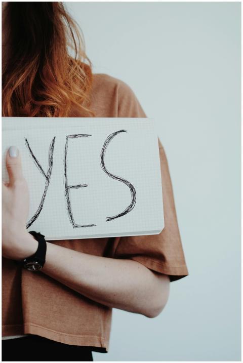 A woman wearing a watch holds a handwritten 'Yes'