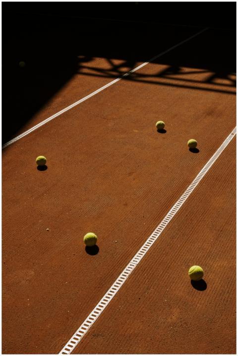 Tennis balls scattered on a sunlit clay court with