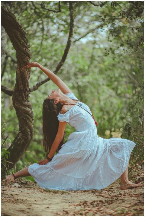 A woman in a white dress performs a yoga pose in a