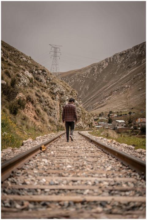 A man in a plaid shirt walks along rustic railroad