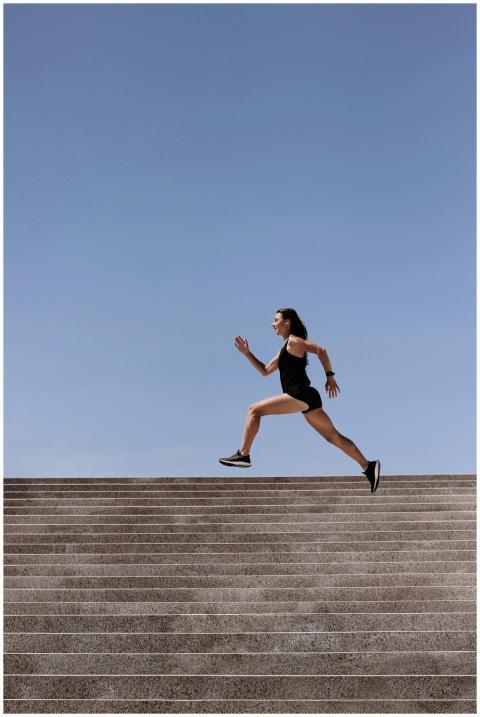 Athletic woman sprinting up outdoor stairs under c