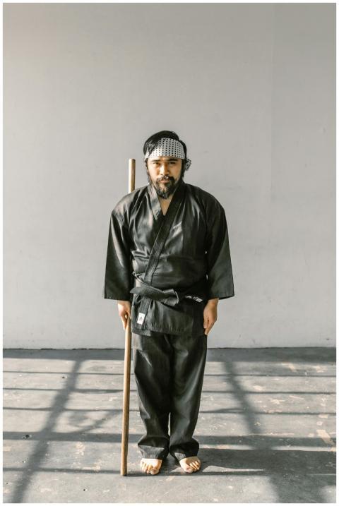 Martial artist posing in black gi with wooden staf